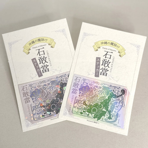 石敢當ステッカーのパッケージ。縦書きの「石敢當」の文字とシーサーの創作イラストが描かれている。シールにはホログラムのフィルムが貼られていて、光に反射して七色に光っている。